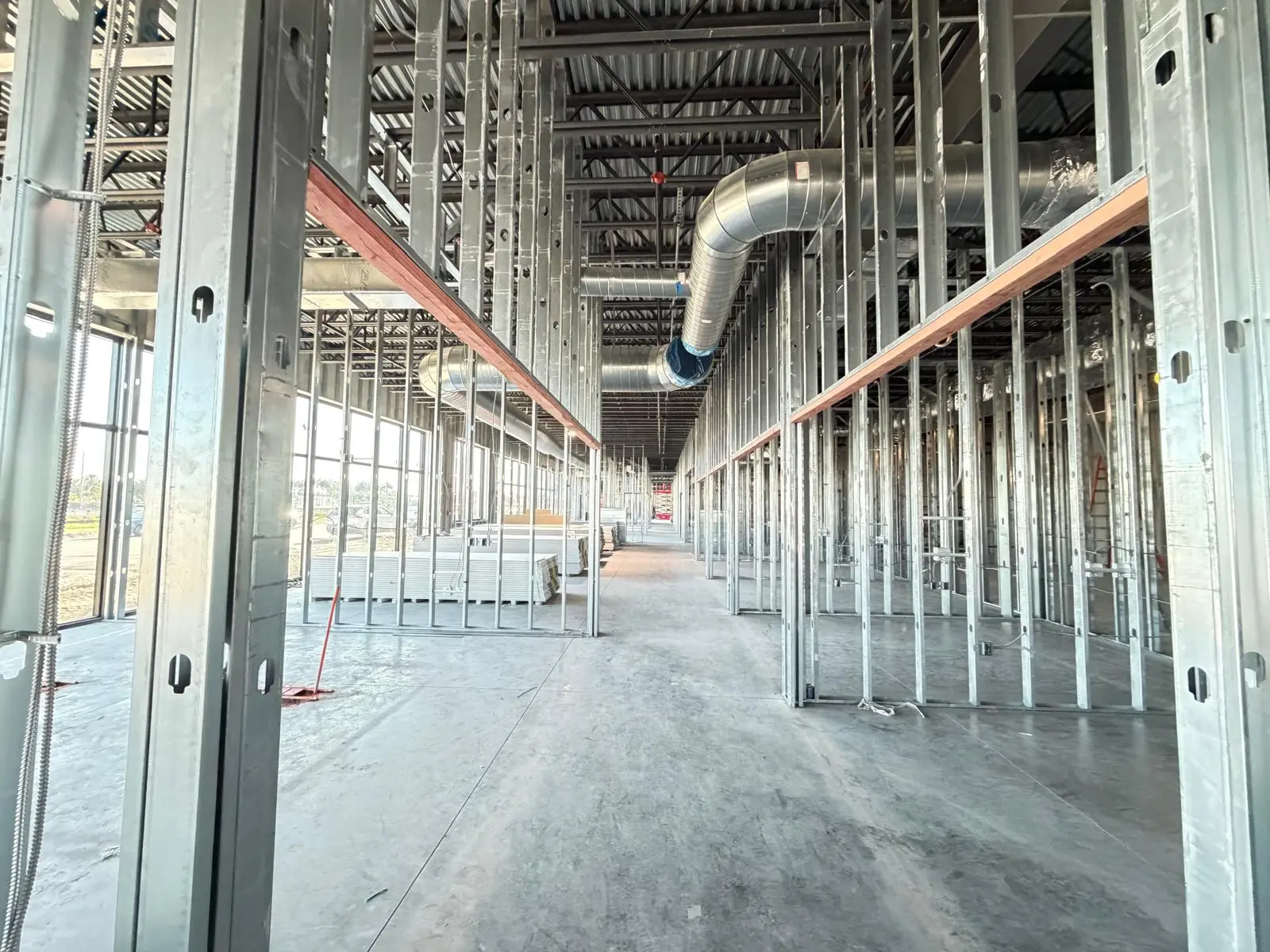 Commercial interior metal stud framing with drywall stacked for installation along a corridor