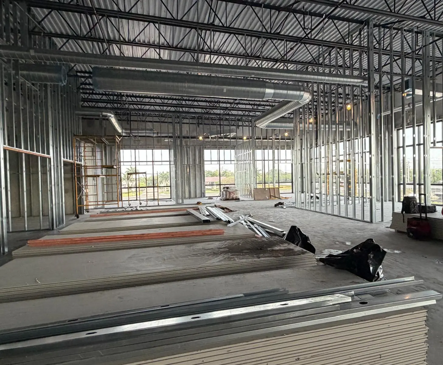 Commercial interior metal stud framing with ductwork, windows, and materials staged for installation